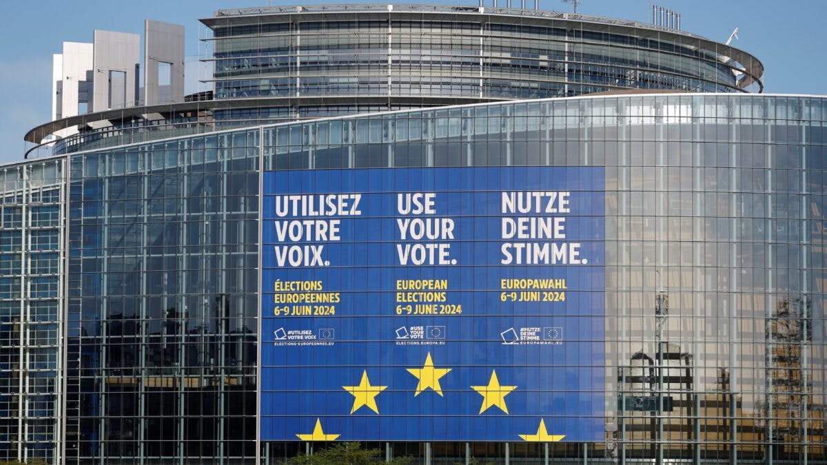 Europeisk parlamentsbygning med bannere som fremmer stemmegivning på flere språk for valget i 2004, omgitt av moderne arkitektur.