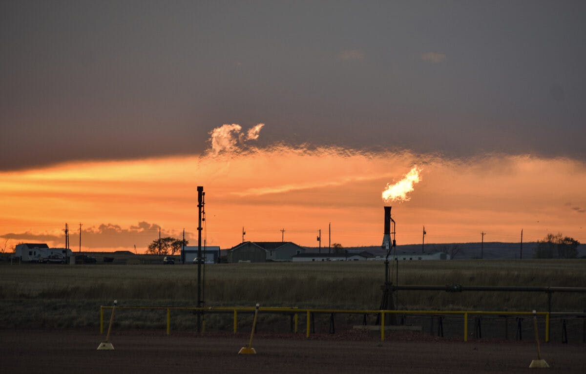Solnedgang over et felt med oljebrønner i bakgrunnen.