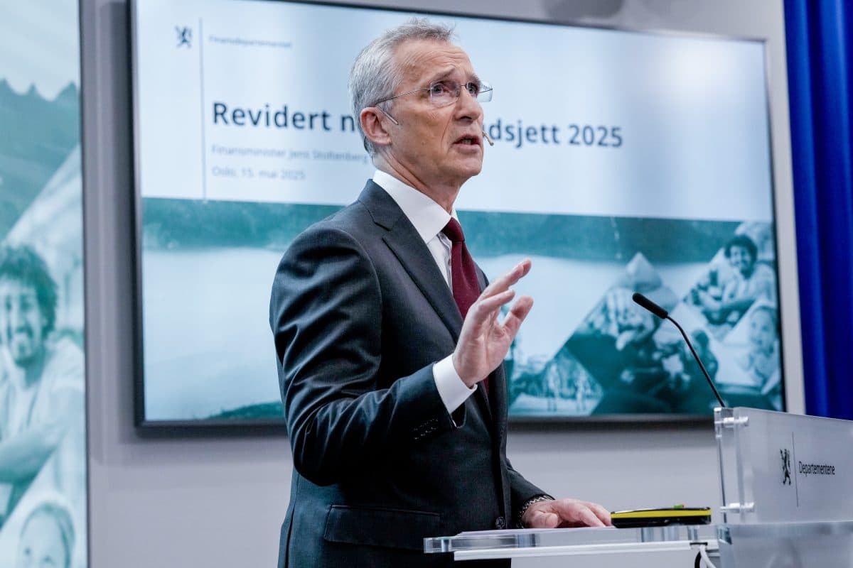 En mann i dress taler på et podium foran en skjerm som viser «Revidert nasjonalbudsjett 2025» og annen tekst på norsk.