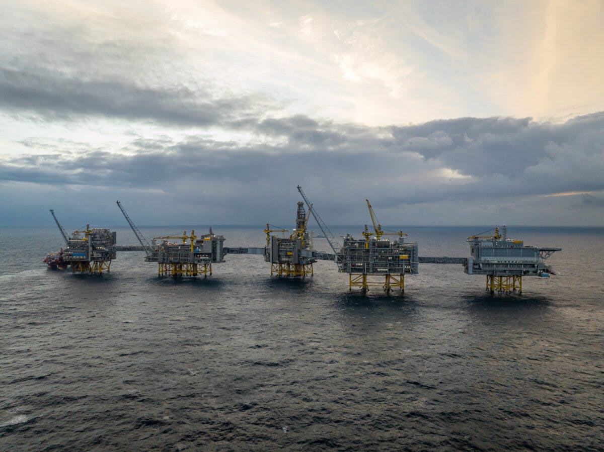 Luftfoto av flere offshore oljeplattformer i havet under en overskyet himmel ved daggry.