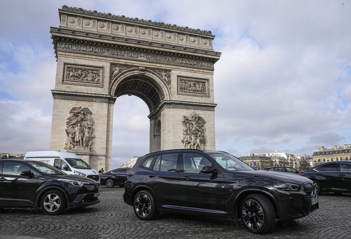 Triumfbuen i Paris, med store biler parkert foran under overskyet himmel.