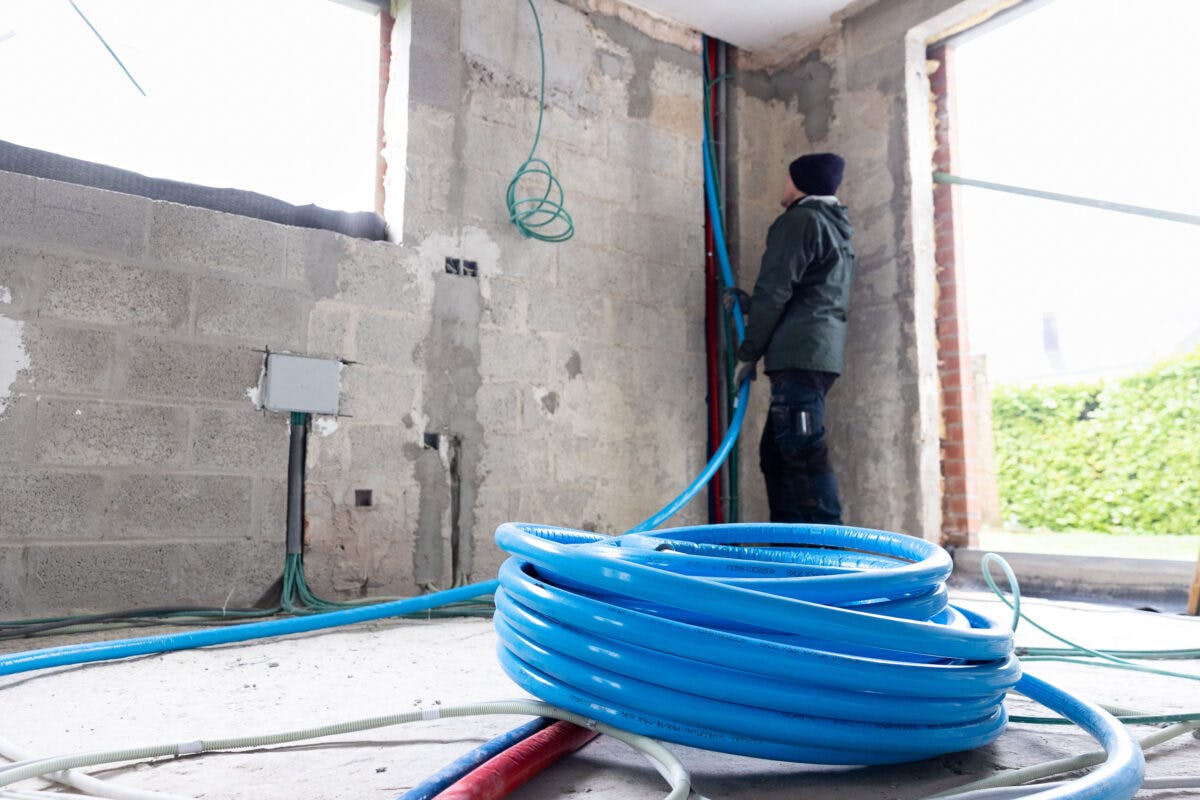 En arbeider installerer blå elektrisk ledning i en delvis konstruert bygning. Kveilet blå ledning ligger på gulvet i nærheten.