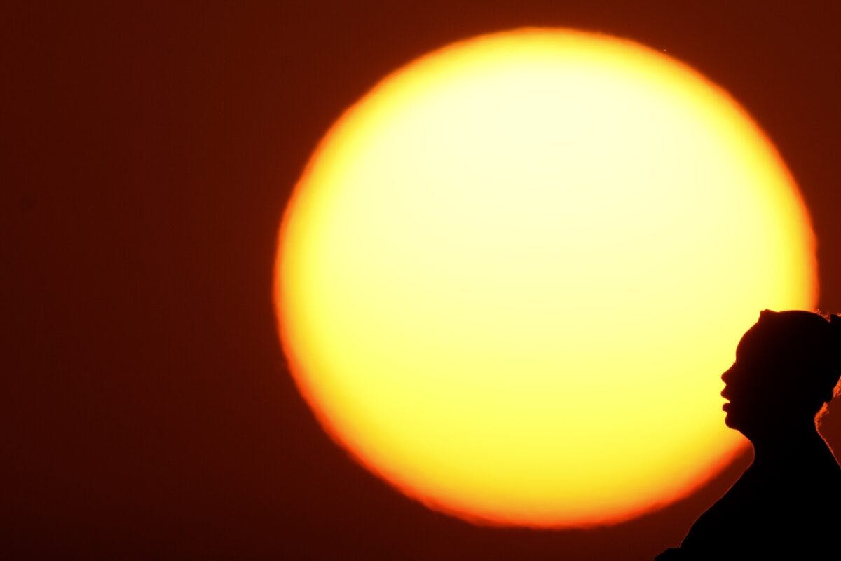 Silhuett av en person mot en stor, knallgul sol under solnedgang.