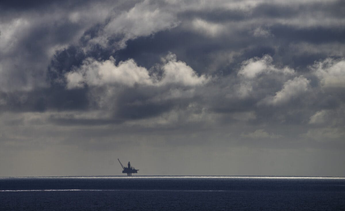 En enslig offshore oljeplattform står i horisonten under en overskyet himmel over et stille hav.