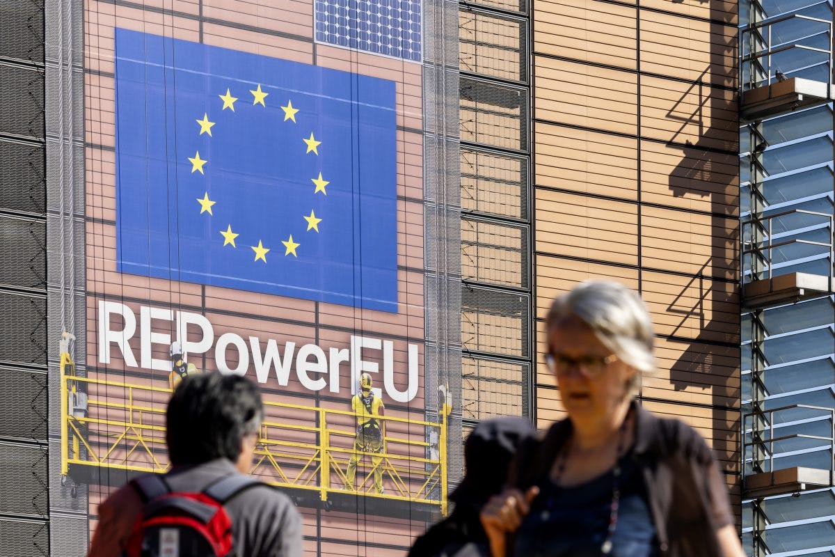 Et stort banner som viser EU-flagget og "REPowerEU" er sett på en bygningsfasade mens folk går forbi i forgrunnen.