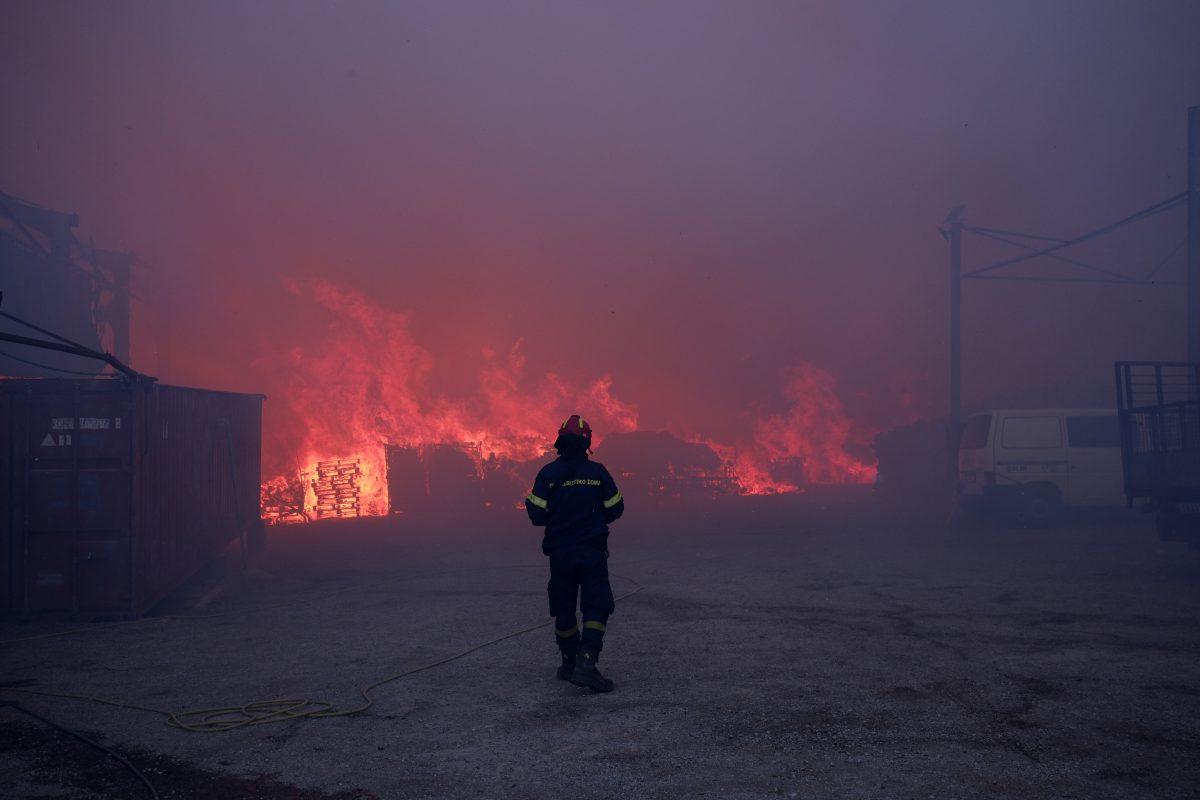 En brannmann møter store flammer og kraftig røyk på et brannsted med containere og en varebil i nærheten.