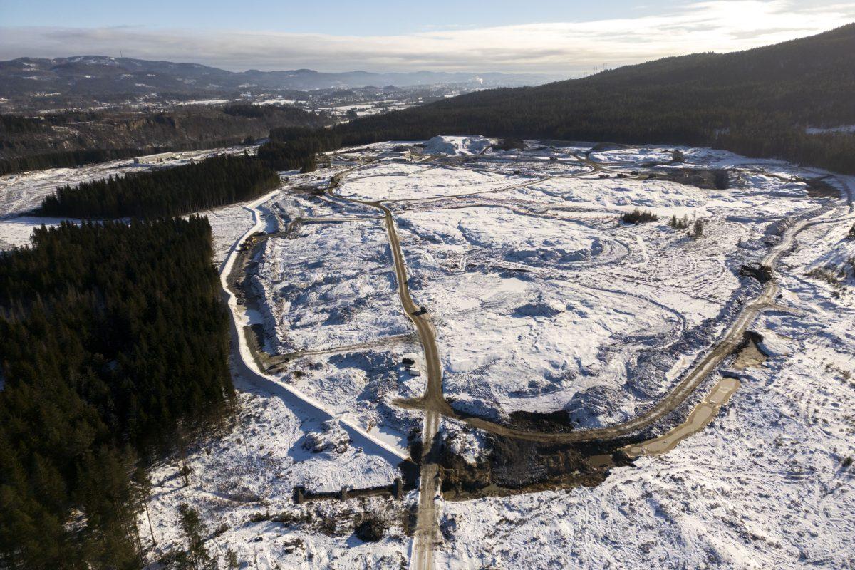 Luftfoto av en stor, snødekt byggeplass omgitt av skog og åser, med veier som snor seg gjennom området.