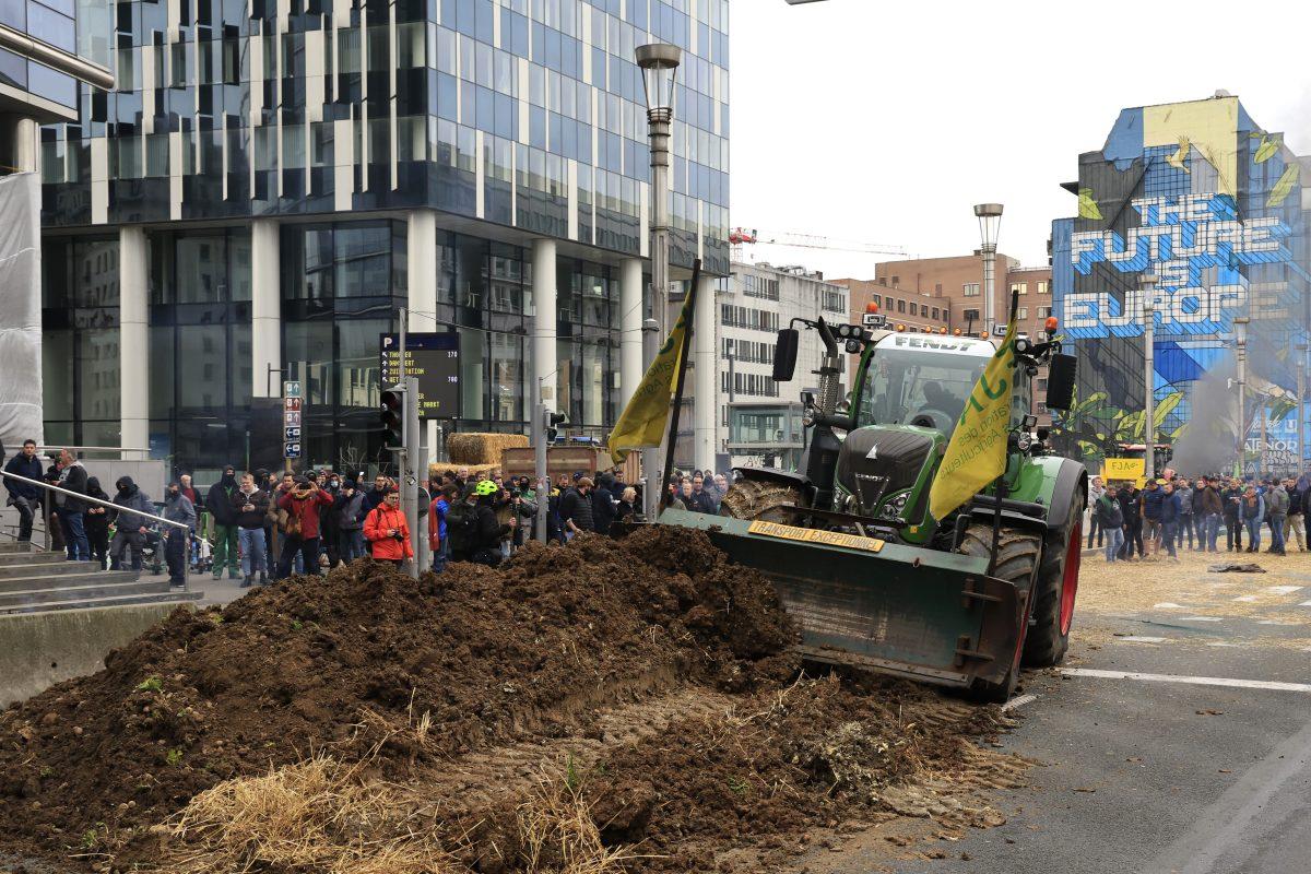 En traktor skyver en haug med skitt midt i en bygate, med en mengde mennesker som observerer og høye bygninger i bakgrunnen. På et veggmaleri på en bygning står det "FRAMTIDEN ER EUROPA".