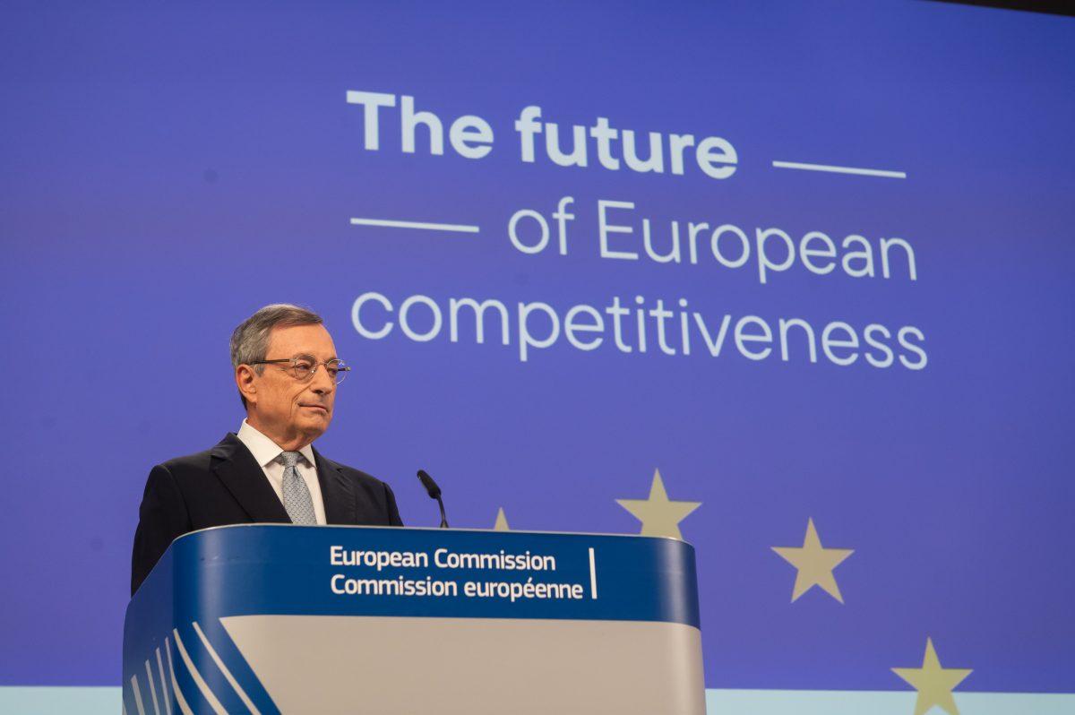 En person står på et podium merket "European Commission" foran et blått bakteppe som leser "The future of European konkurranseevne.