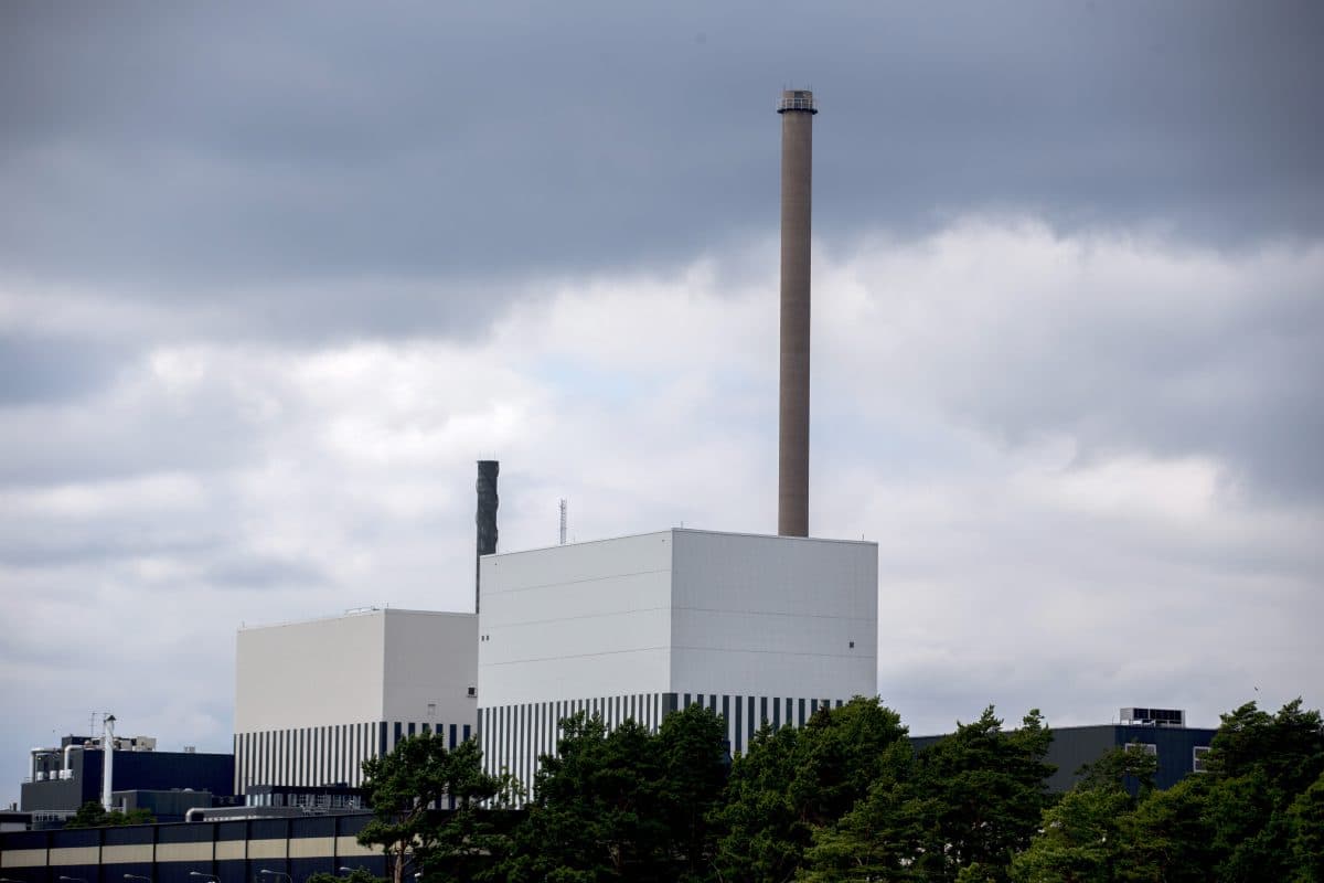 Et kraftverk med to store, rektangulære bygninger og høye skorsteiner under overskyet himmel, omgitt av trær.