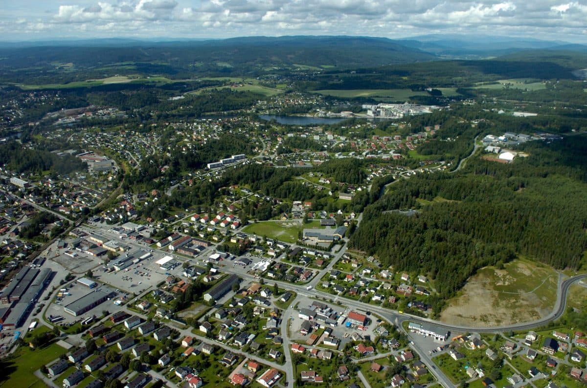 Luftfoto av et forstadsområde med en blanding av bolighus, veier og skogkledde områder på en delvis overskyet dag.