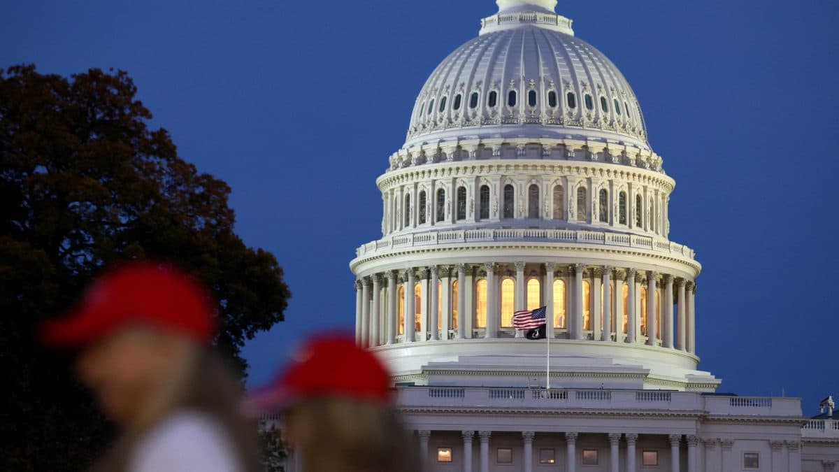 U.S. Capitol-bygningen i skumringen med to personer i røde luer i forgrunnen.