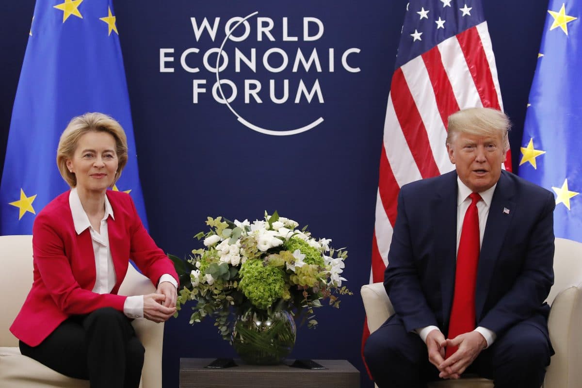 To personer sitter i stoler med flagg og et "World Economic Forum"-bakteppe. Et blomsterarrangement er plassert mellom dem.