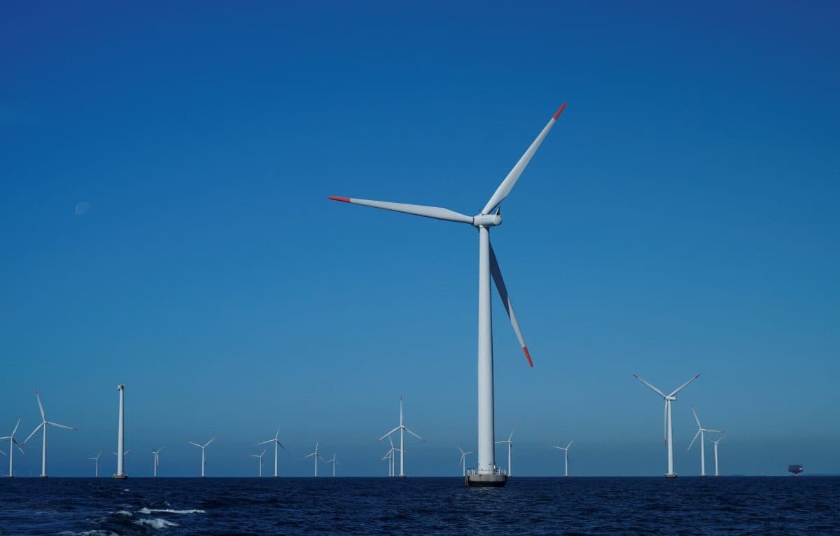 En gruppe vindturbiner står i havet under en klarblå himmel.