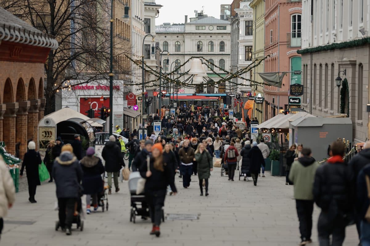 En travel bygate med mange fotgjengere, dekorert med festlige hengelys. Bygninger ligger langs begge sider, og en trikk er synlig i det fjerne.