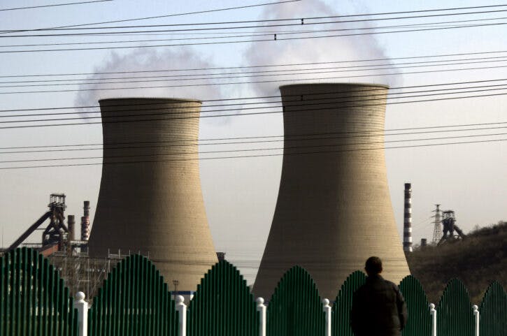 A man looks over a fence towards chimneys of a coal-burning power station located on the outskirts of Beijing