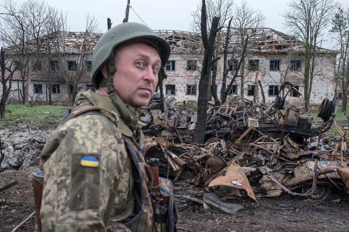 Ukrainsk soldat foran ødelagte militærkjøretøy og utbombet hus