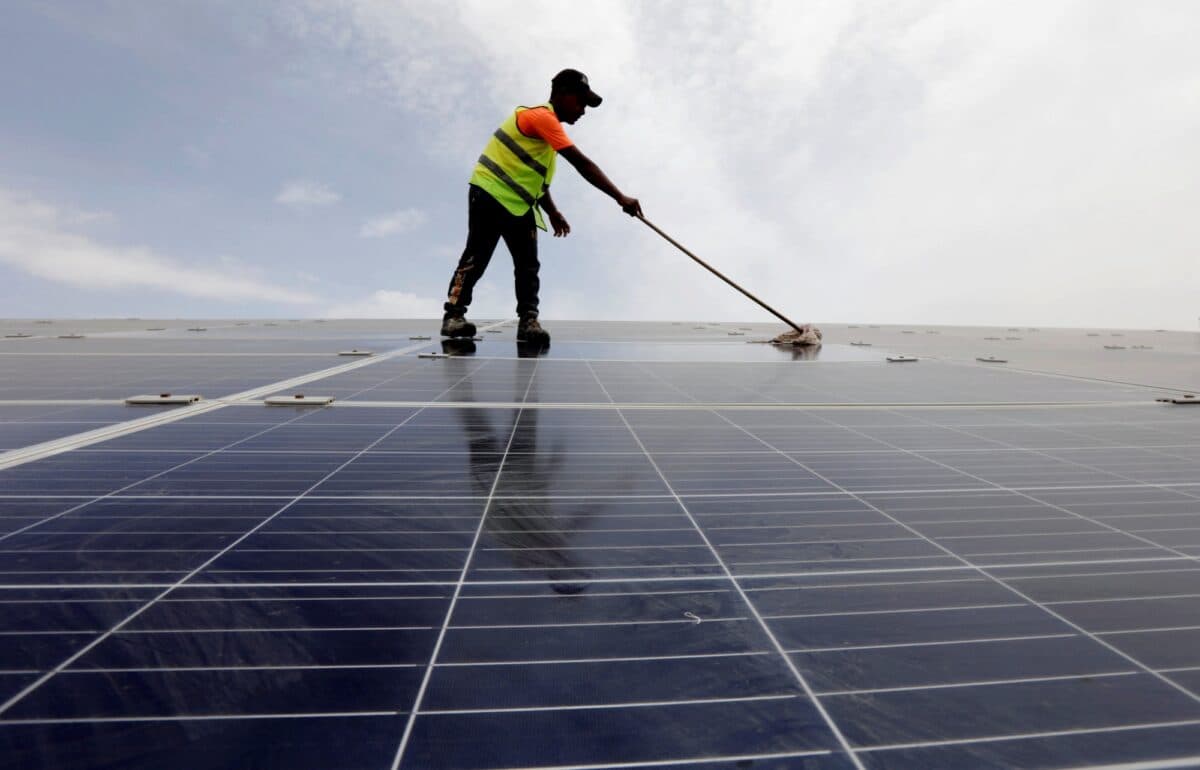 Mann rengjør solcellepaneler med kost.
