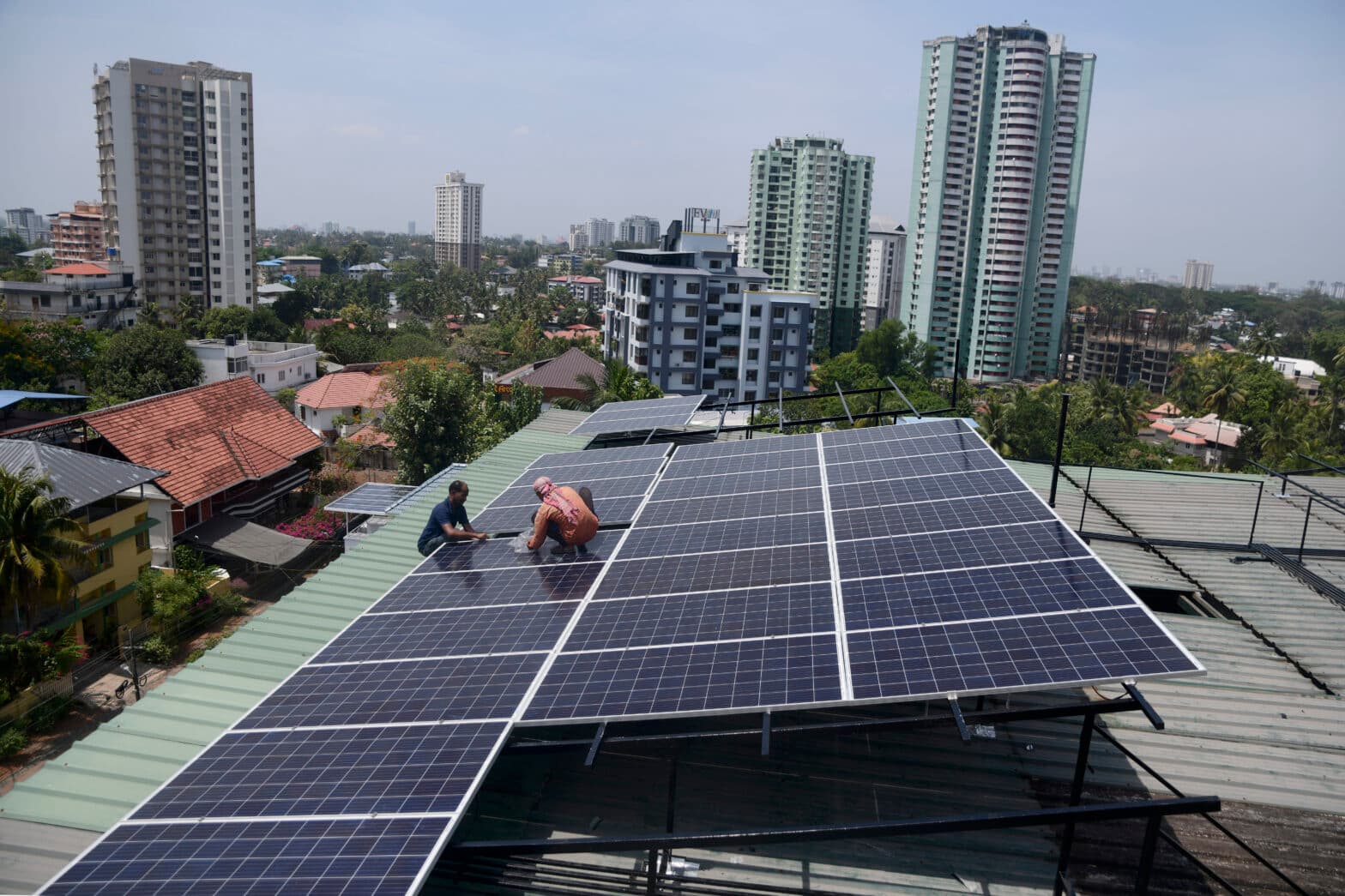 Arbeidere jobber med solceller på toppen av et bygg i en by