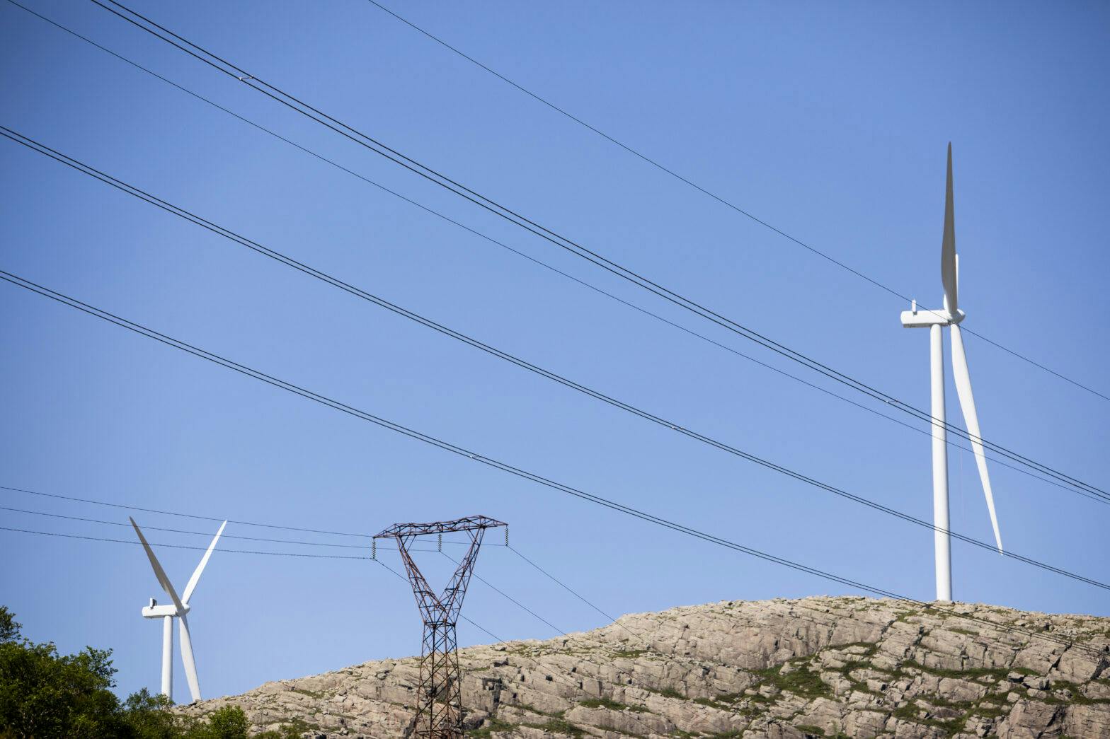 Vindturbiner og strømmaster på et fjell mot blå himmel