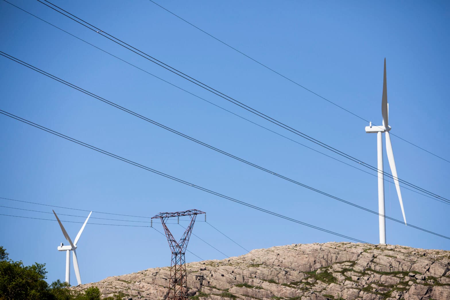 Vindturbiner og strømmaster på et fjell mot blå himmel