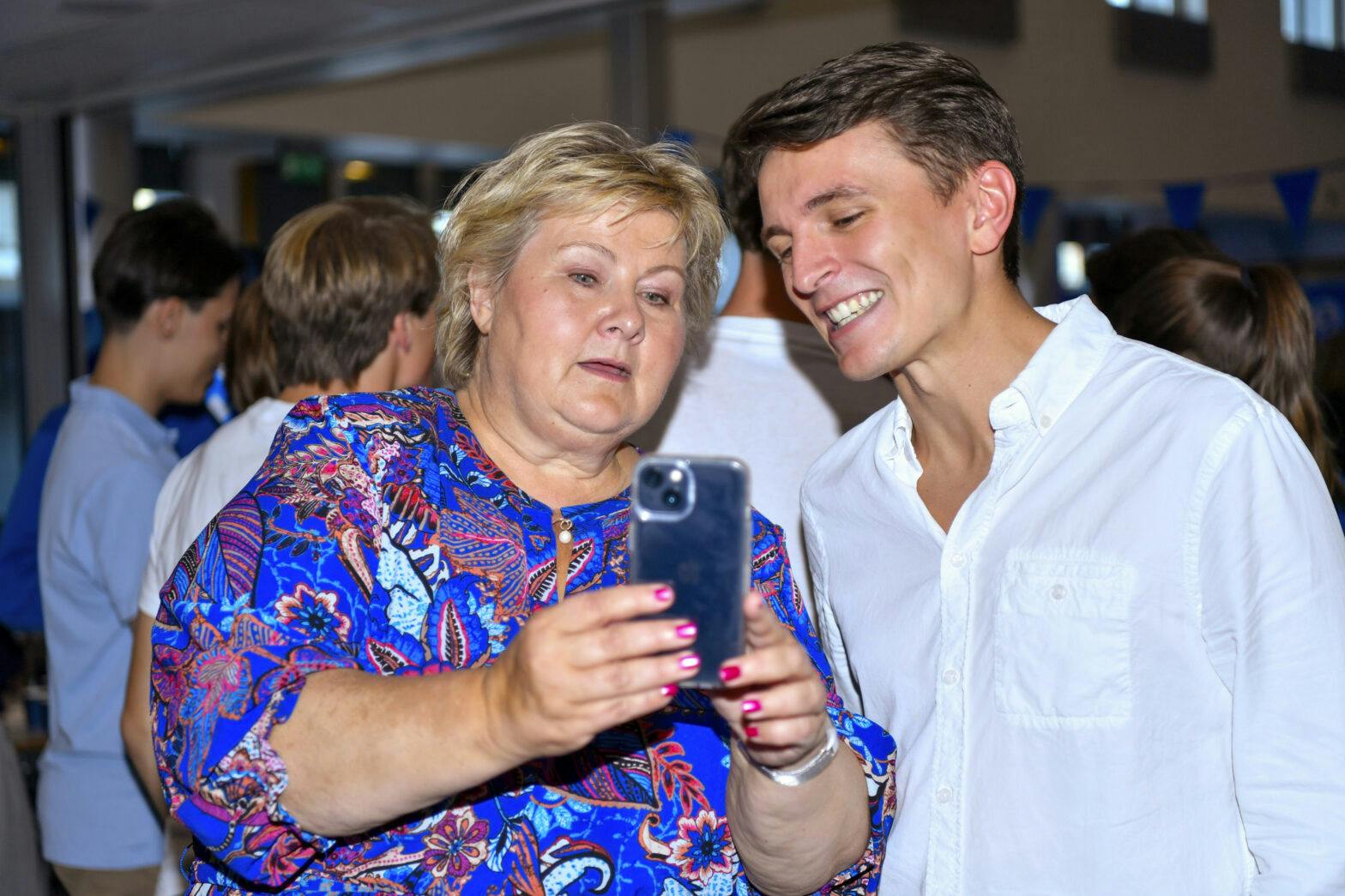 En kvinne iført en blå skjorte og en ung mann ser på en mobiltelefon.