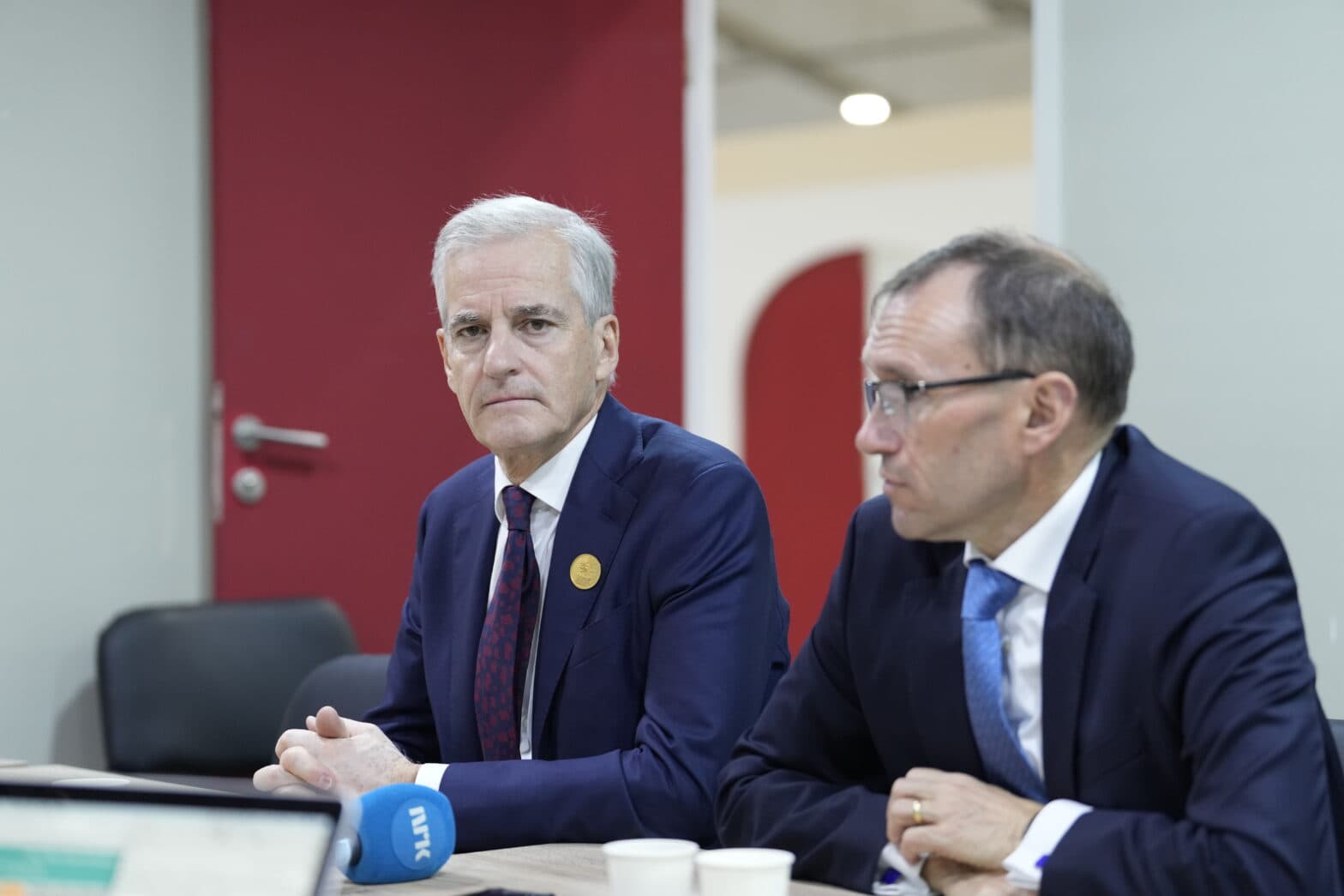 To menn i dress sitter ved et bord.