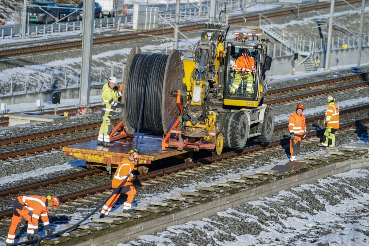 Arbeidere legger kabel langs jernbaneskinner.