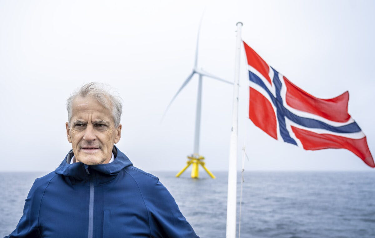 En mann som står foran en vindturbin med et norsk flagg.
