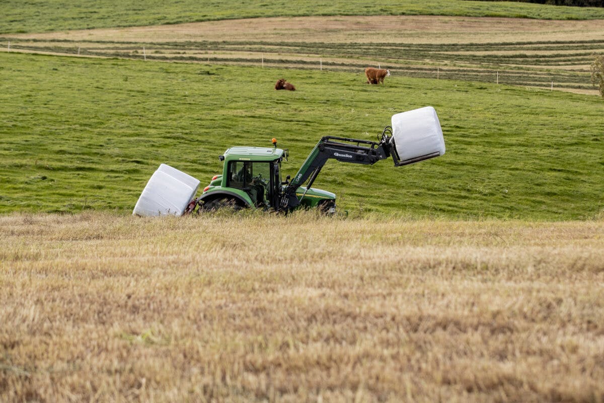 En traktor trekker en høyballe på et jorde.