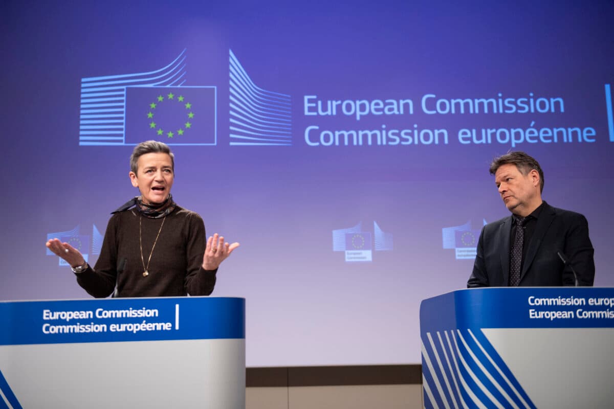 To personer står ved podier foran et skilt fra Europakommisjonen.