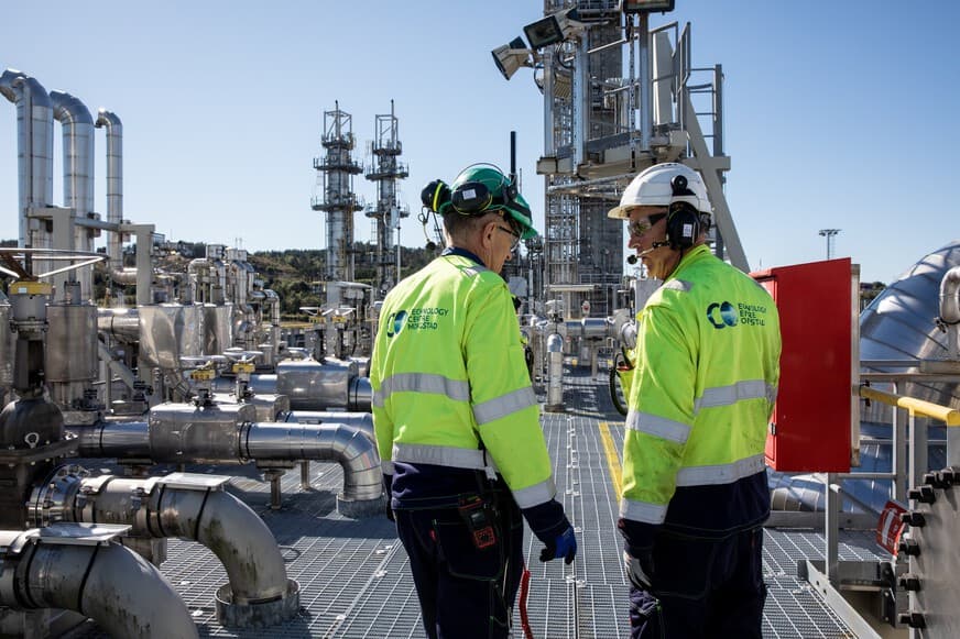 To arbeidere som står foran et oljeraffineri.