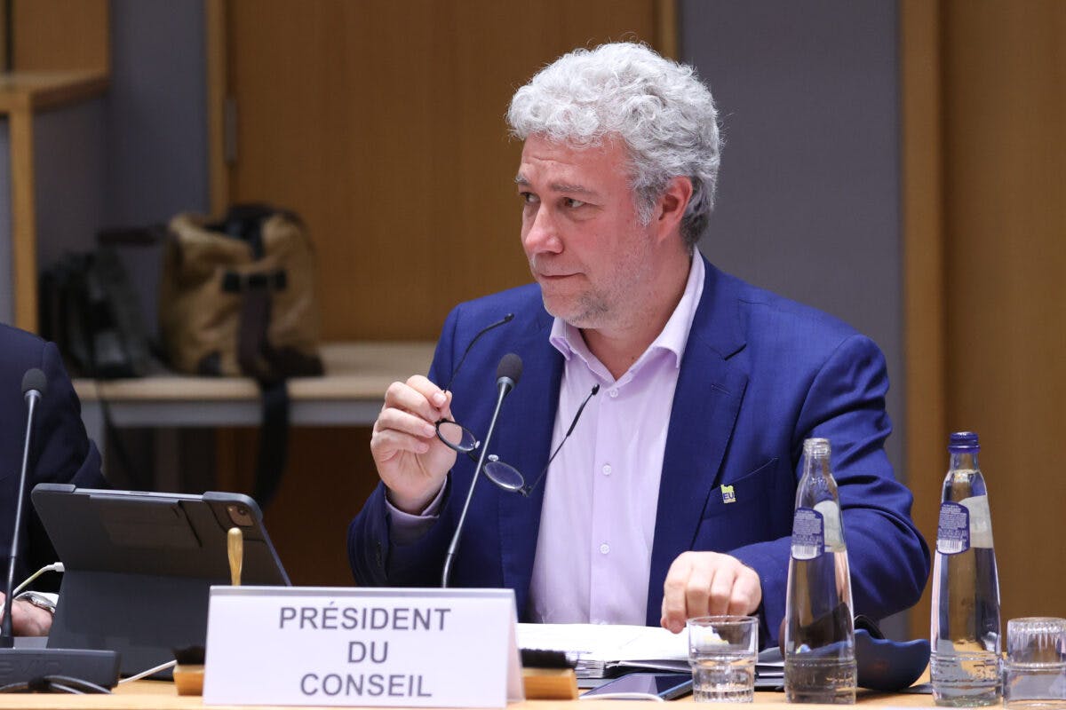 En mann i blå dress sitter ved et konferansebord med en mikrofon og et navneskilt der det står "président du conseil.