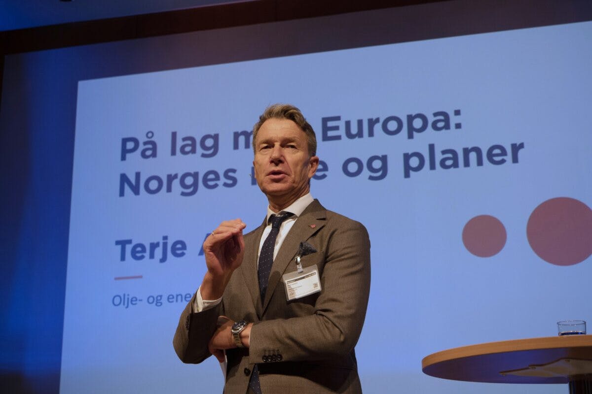 En dresskledd mann presenterer på en konferanse med en prosjektert presentasjon i bakgrunnen med tittelen «på lag med europa: norges strategi og planer.