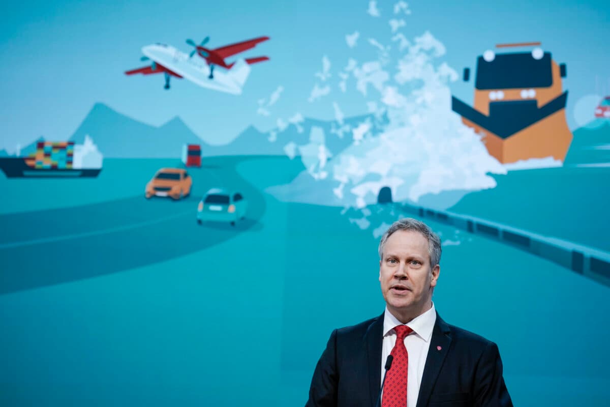 En mann som leverer en presentasjon med en grafisk bakgrunn som viser ulike transportmåter.