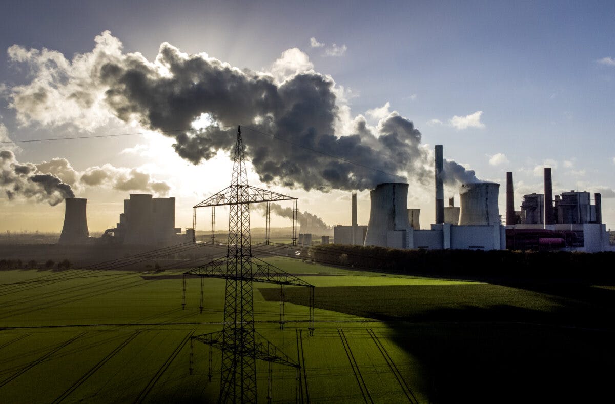 Industrielt kraftverk som avgir røyk med et overføringstårn i forgrunnen.