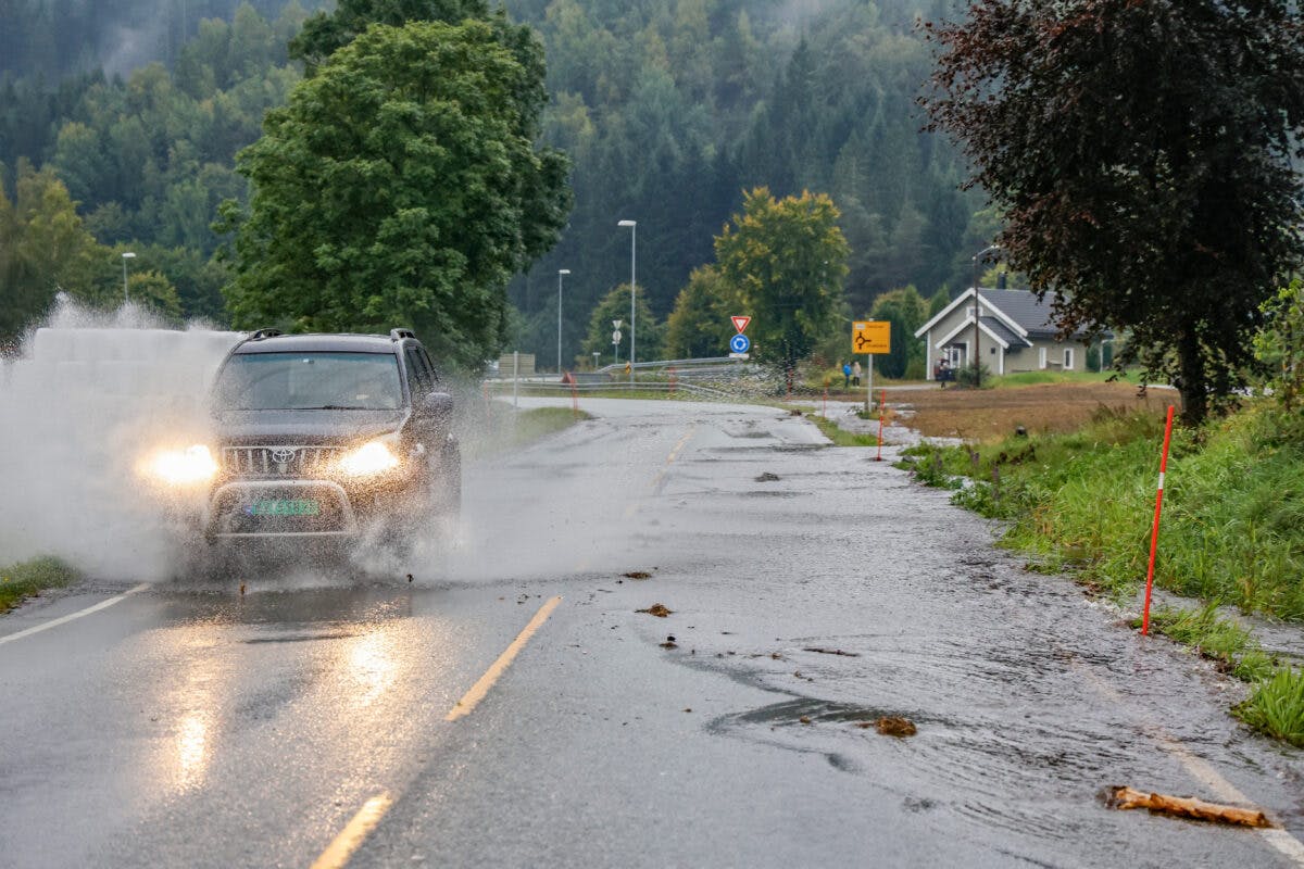 Bil kjører gjennom en oversvømt gate etter kraftig regn.