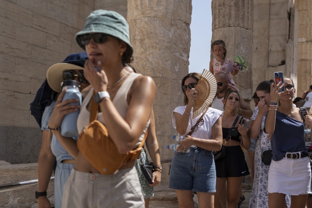 Turister med vannflasker som utforsker et solfylt historisk sted, noen bruker smarttelefoner til bilder.