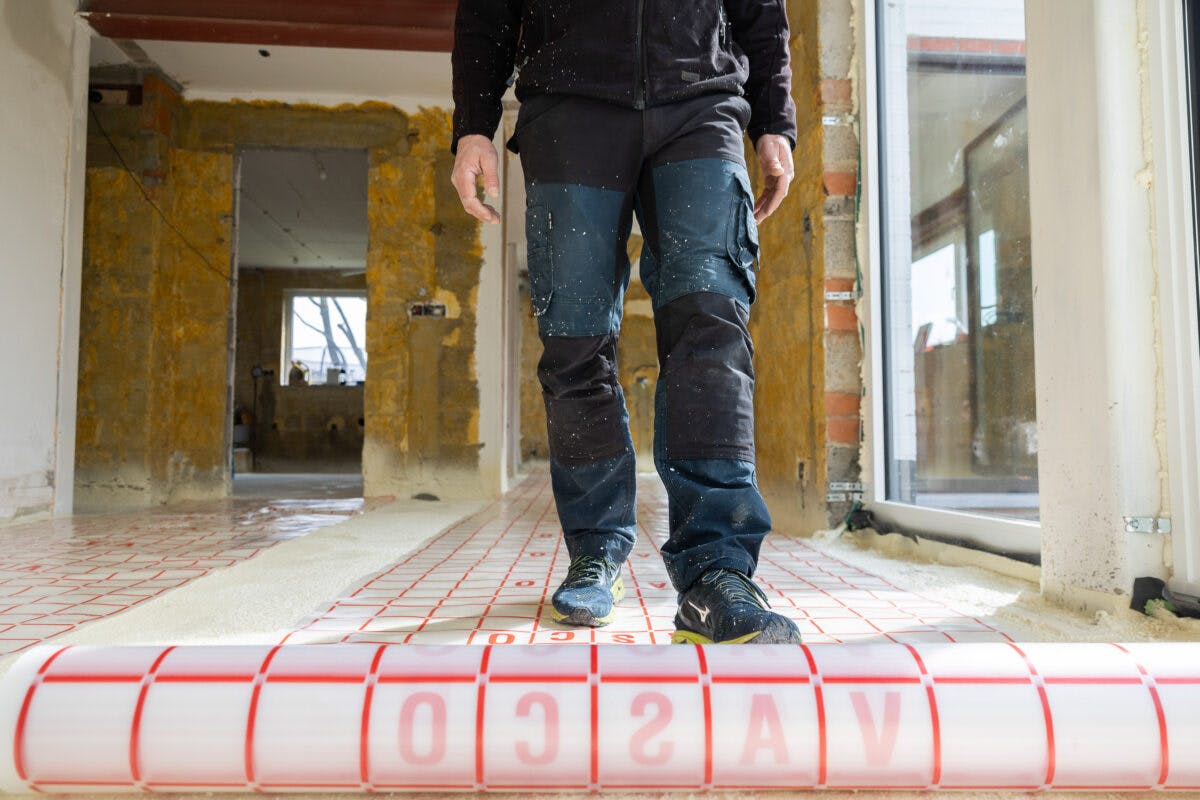 En bygningsarbeider som står på et nylig installert rødt gulvvarmesystem i en bygning under renovering.