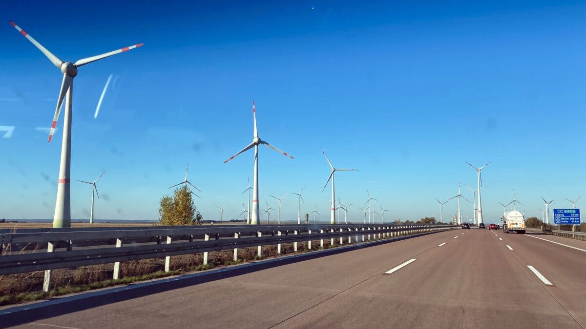 Motorvei omkranset av roterende vindturbiner under en klar blå himmel.