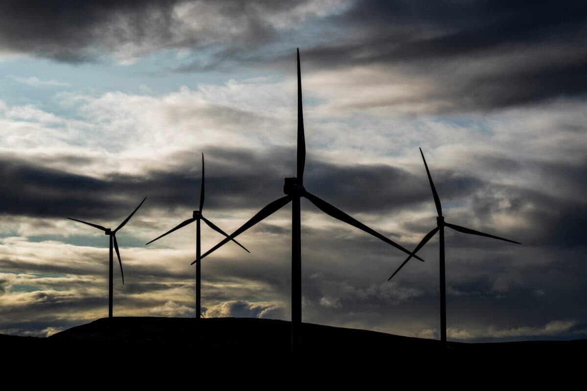 Fire vindturbiner står i et kupert landskap under en overskyet himmel, silhuettert mot det falmende dagslyset.