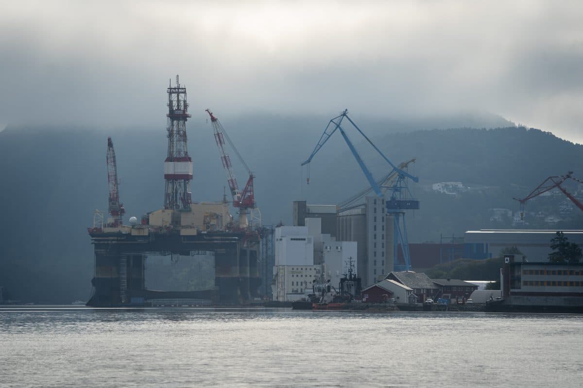 Offshore oljerigg i et verft med kraner, omgitt av tåkete fjell og stille vann.