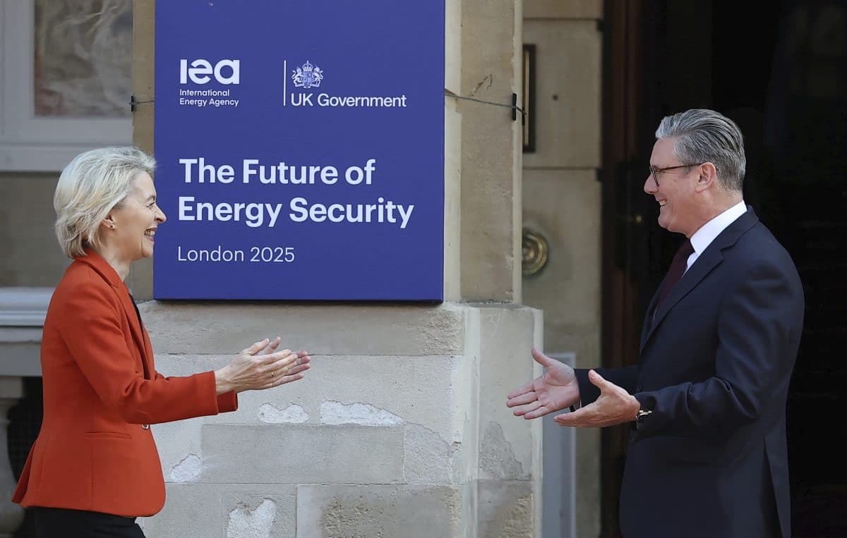 To personer i forretningsantrekk hilser på hverandre utenfor en bygning med et skilt med teksten «The Future of Energy Security, London 2025», arrangert av IEA og den britiske regjeringen.