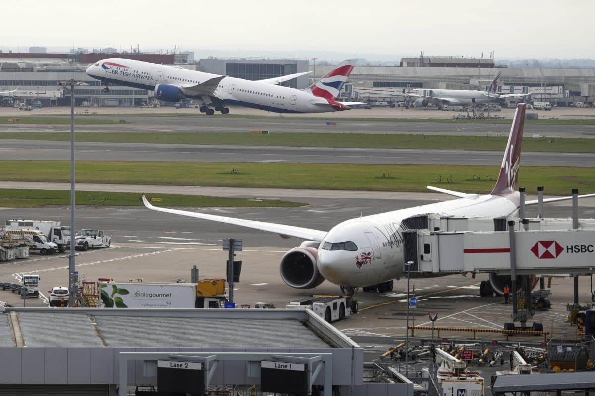 Et British Airways-fly tar av mens et Virgin Atlantic-fly står parkert ved en gate på en flyplass, med servicebiler og andre fly i bakgrunnen.