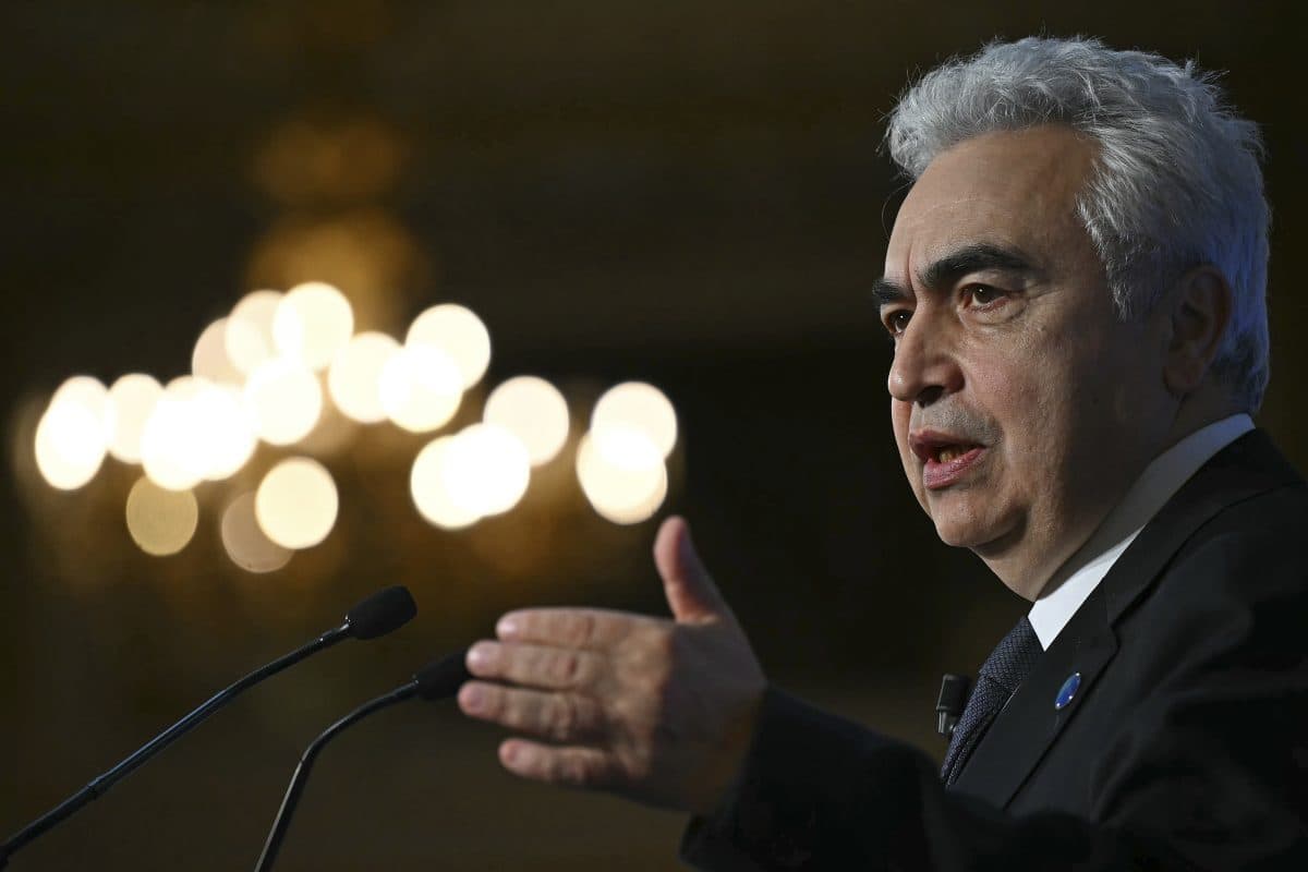 En mann med grått hår gestikulerer mens han snakker i en mikrofon, med en uskarp lysekrone i bakgrunnen.