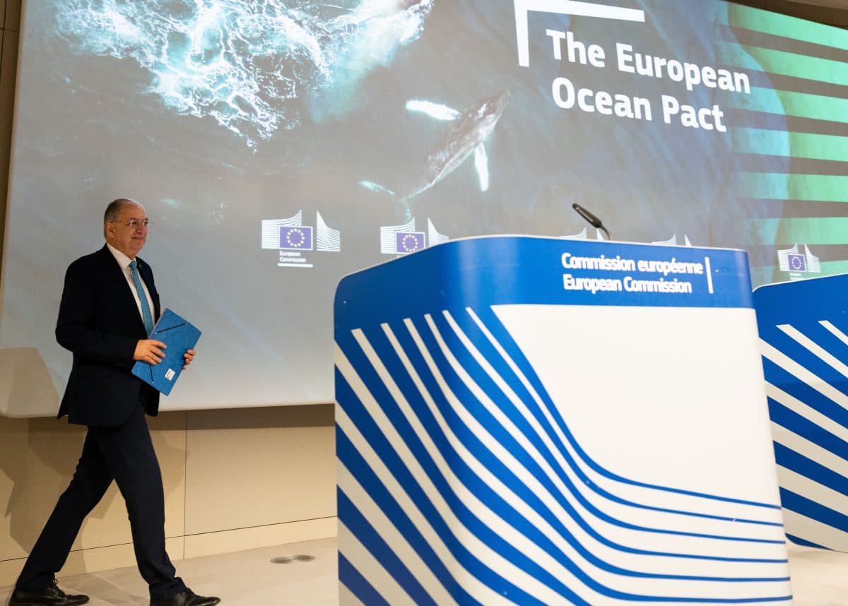 En mann går mot et podium som viser EU-kommisjonens logo, med en skjerm bak seg som sier «Den europeiske havpakten» og viser et bilde av havet og en hval.