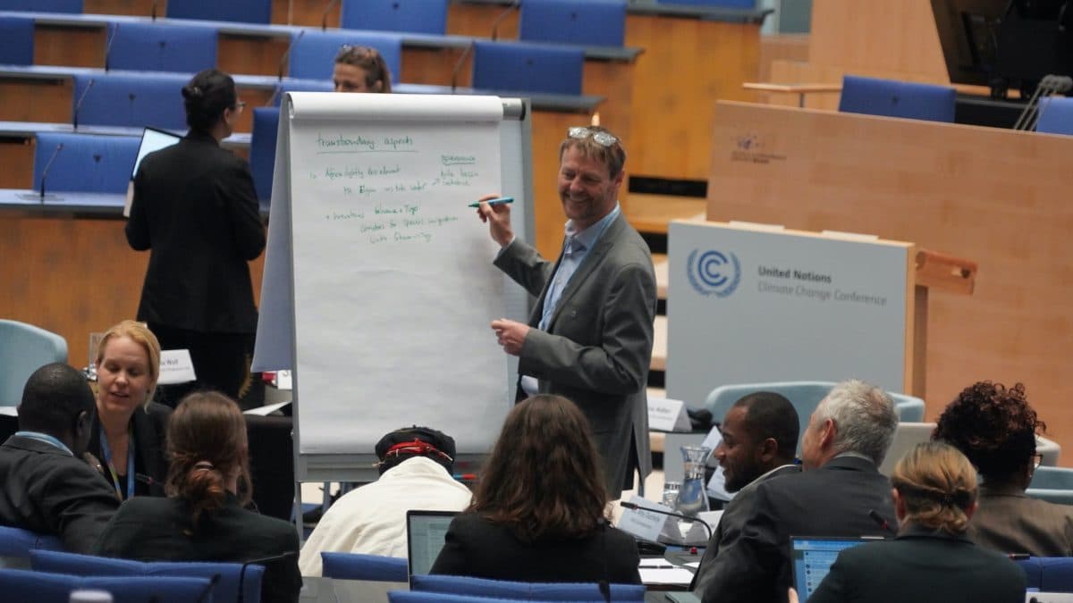 En mann skriver på et stort ark under en gruppediskusjon på en FN-klimakonferanse i et moderne konferanserom.