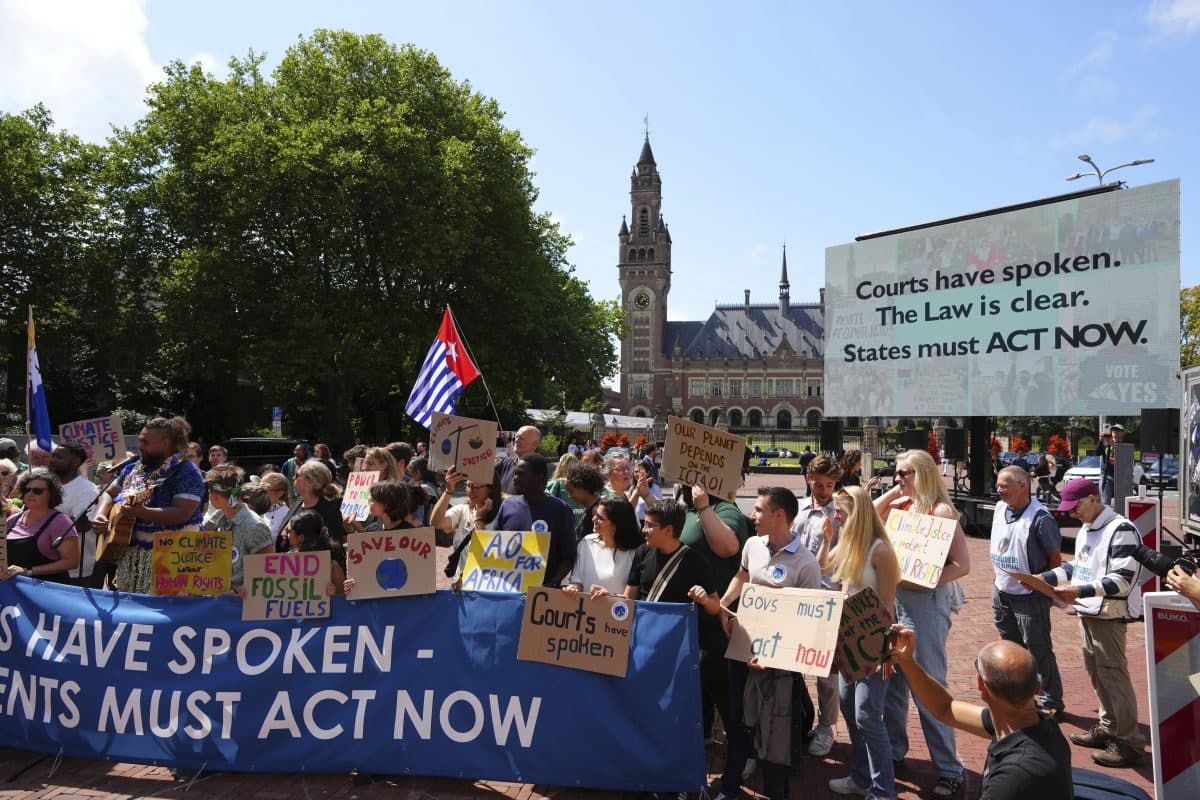 En gruppe mennesker protesterer utenfor en historisk bygning med skilt om klimatiltak; på en stor plakat står det: "Domstolene har talt. Loven er klar. Statene må HANDLE NÅ.