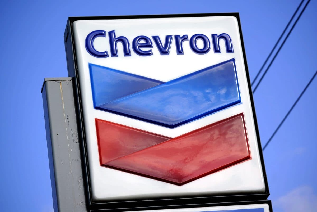 Opplyst Chevron-bensinstasjonsskilt med blå og rød chevronlogo mot en blå himmelbakgrunn.