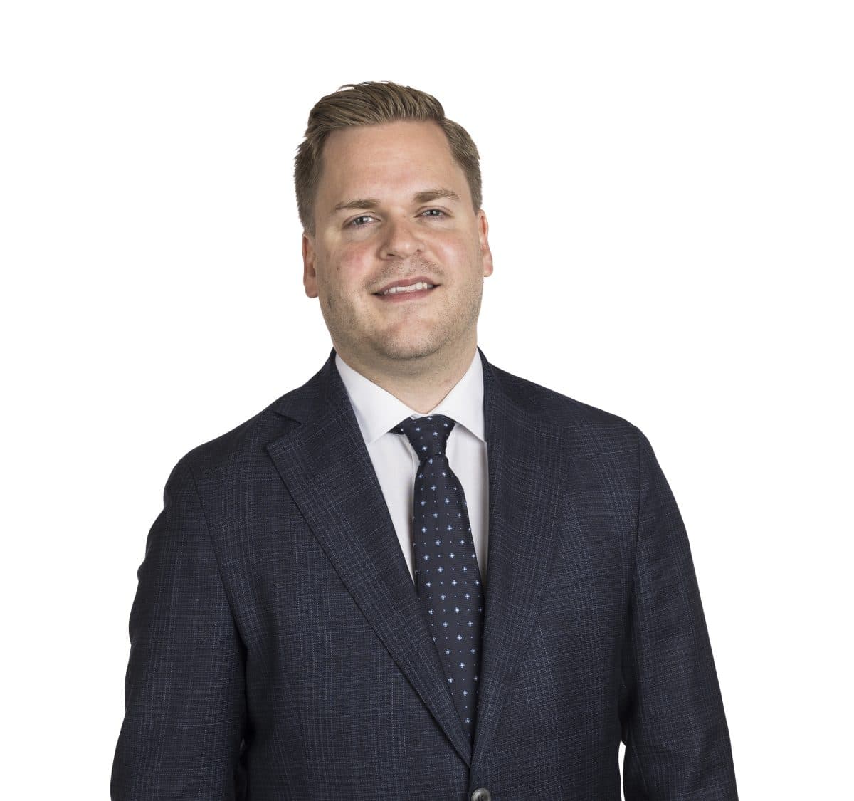 En mann iført mørk rutete dress, hvit skjorte og mørkprikkete slips står smilende mot en hvit bakgrunn.